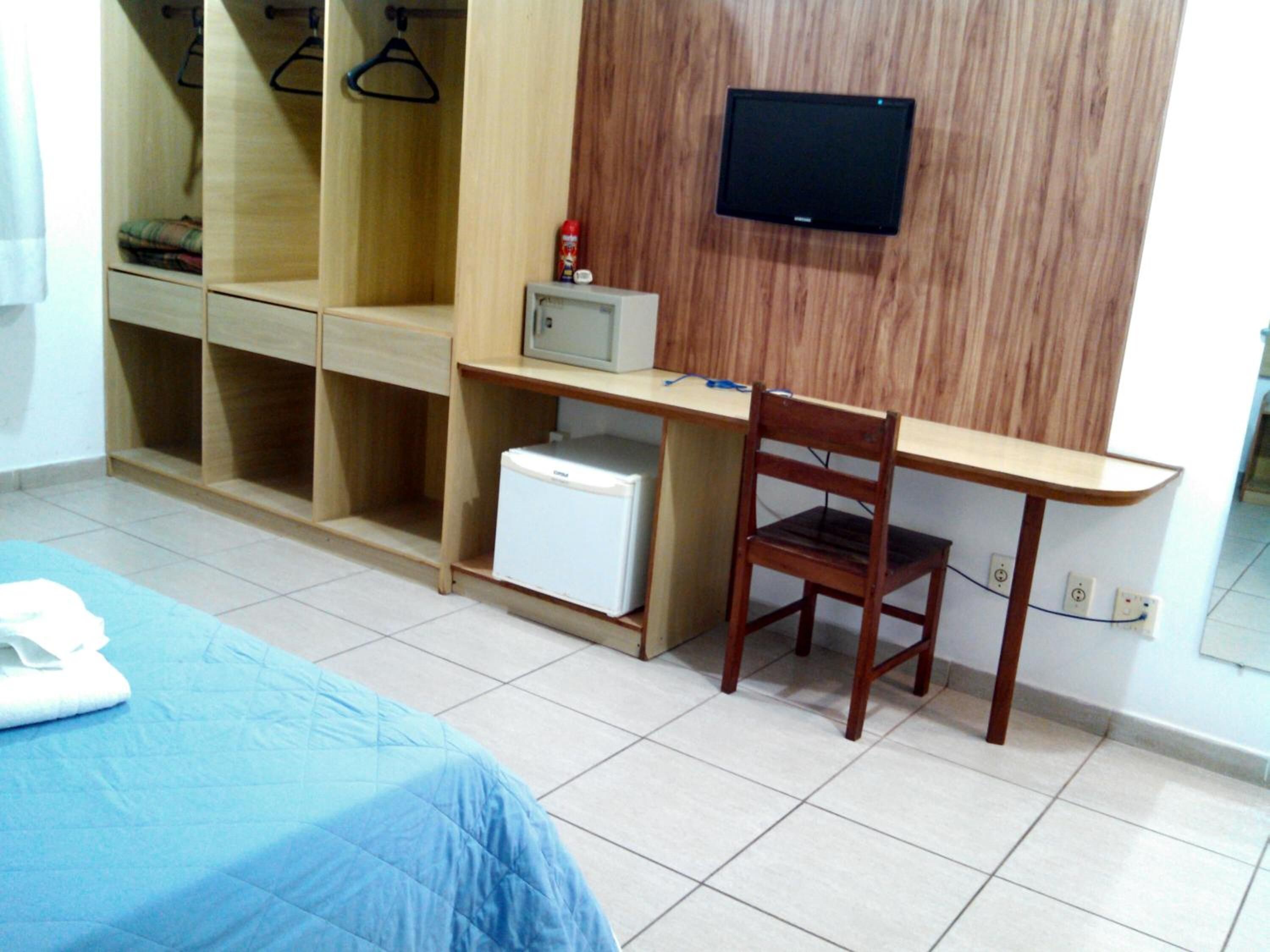 Une petite chambre comprenant un lit, un bureau, une chaise, un petit réfrigérateur et un téléviseur fixé au mur.