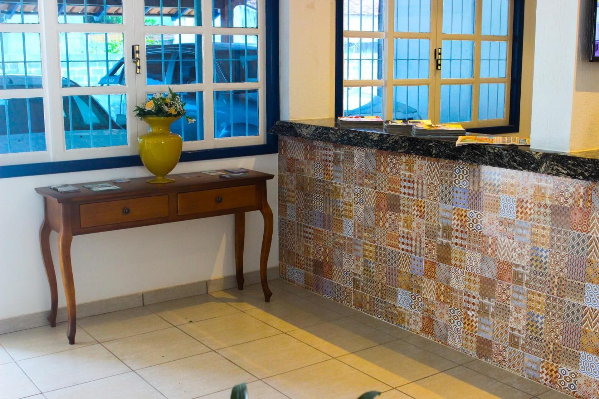 Uma cozinha com painel de azulejos, uma mesa de madeira com um vaso e uma janela com persianas.