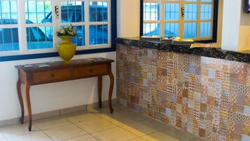 Uma cozinha com painel de azulejos, uma mesa de madeira com um vaso e uma janela com persianas.