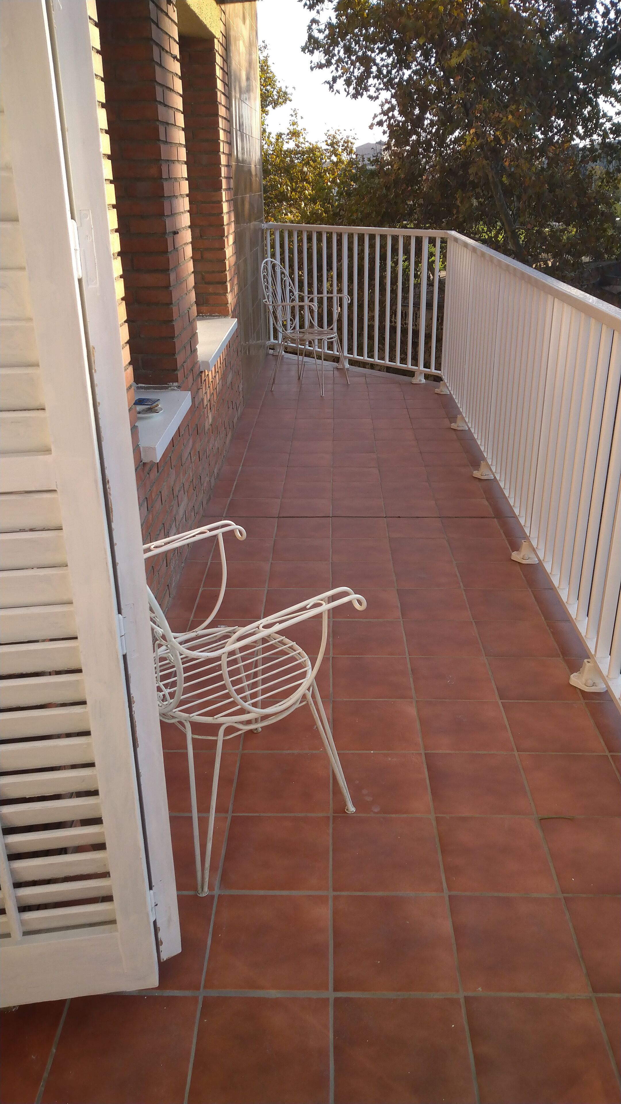 A balcony with terracotta tiles, white metal chairs, and a white railing.