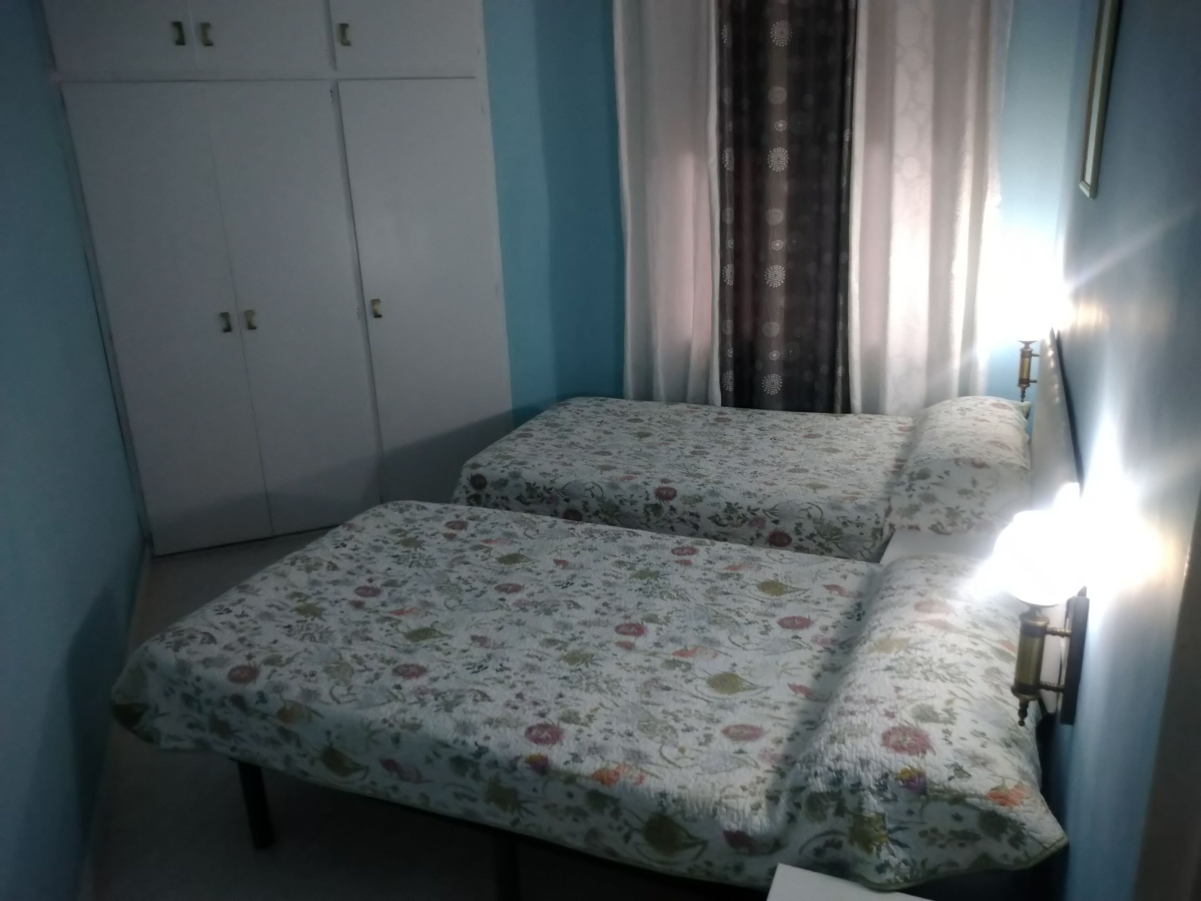 Une chambre avec deux lits, une armoire et une lampe fixée au mur.