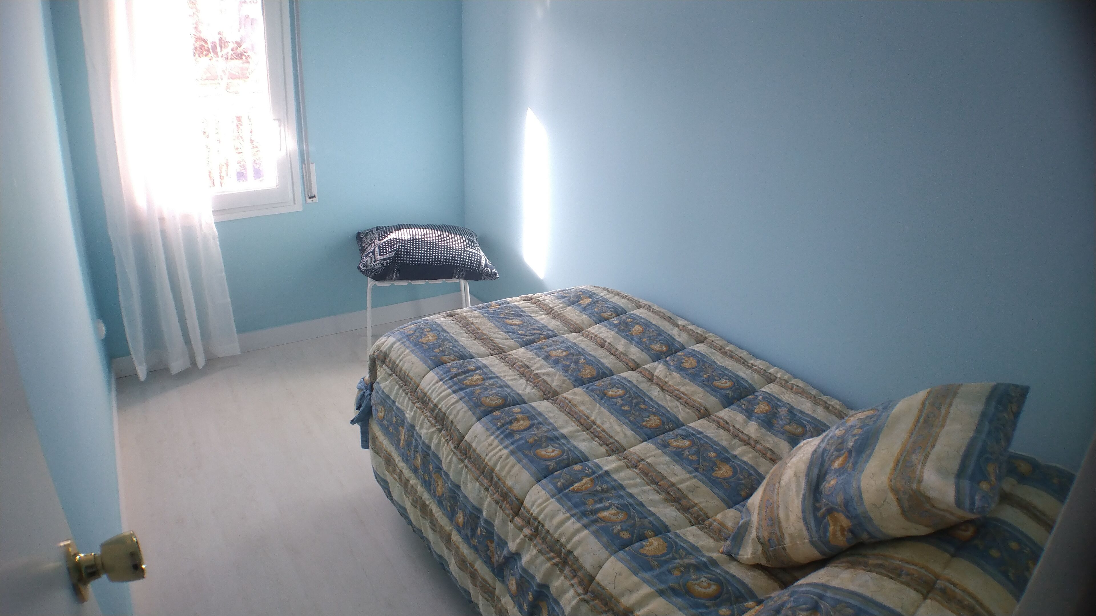 Een slaapkamer met een bed, een stoel en een raam met gordijnen.