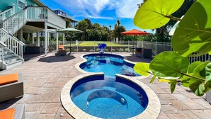 A swimming pool with a curved design, surrounded by a stone deck and outdoor furniture. - Pet-Friendly Island Home | Pool, Hot Tub + Cart (Upper Captiva)
