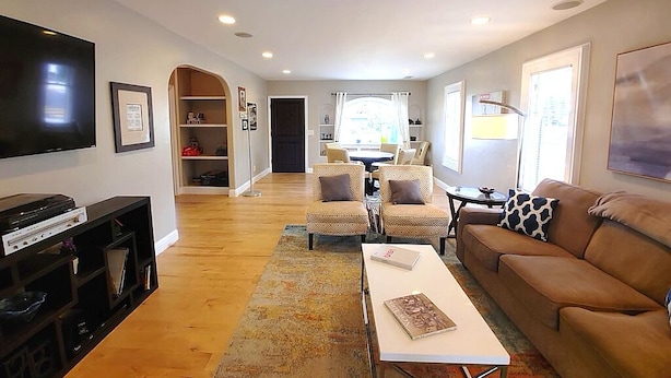 A living room with a flat-screen TV, a sofa, a coffee table, and a dining area with chairs.