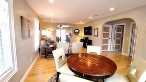 A dining area with a round wooden table and white chairs, a kitchen in the background, and a hallway leading to a door.