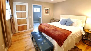 A bedroom with a large bed, a bench, a bedside table, and a door leading to another room.