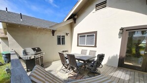 A patio with a grill, dining table, chairs, and a cushioned lounge area.