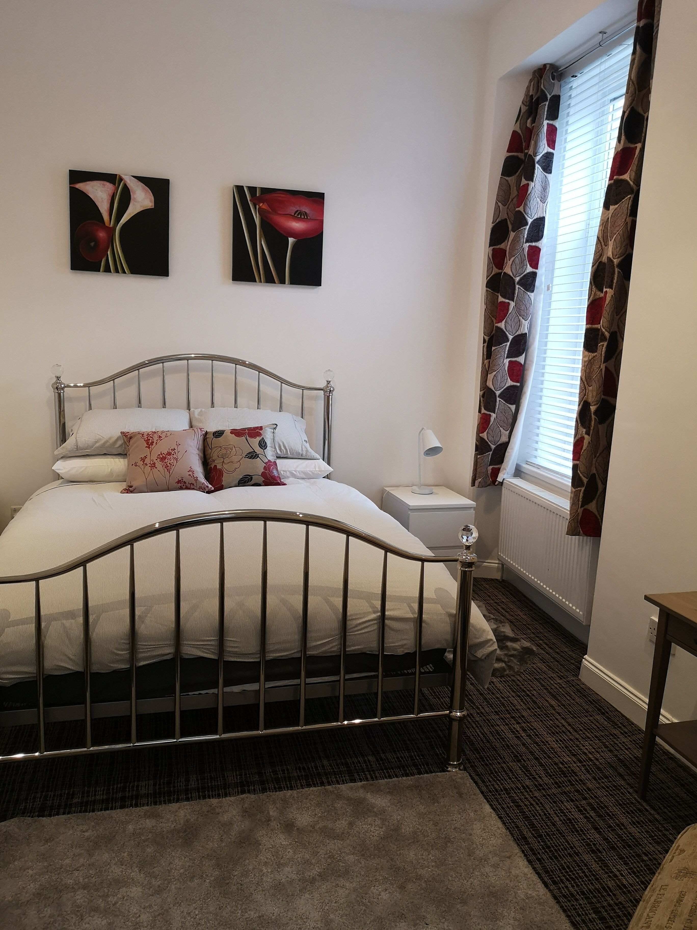 A neatly arranged bedroom with a metal-framed bed, white bedding, and two floral wall art pieces.