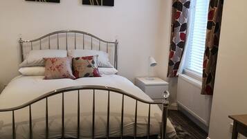 A neatly arranged bedroom with a metal-framed bed, white bedding, and two floral wall art pieces.