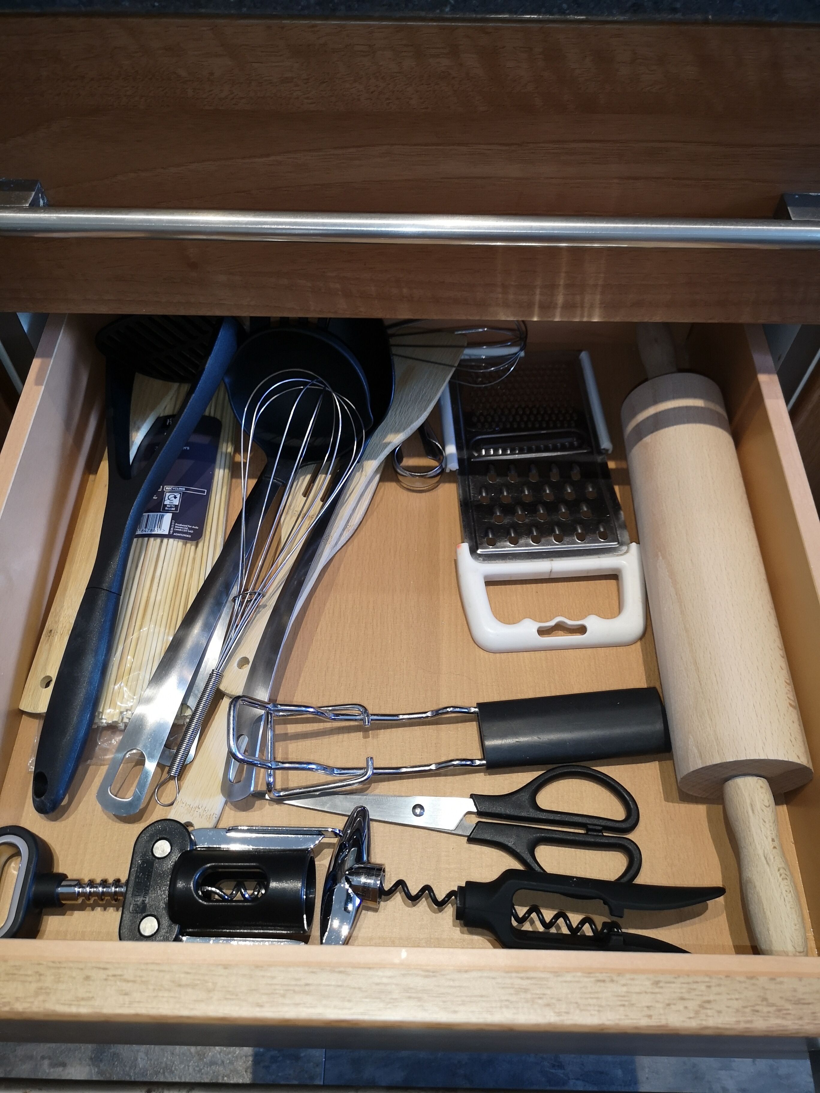 A drawer containing kitchen utensils including whisks, a grater, a rolling pin, and a corkscrew.