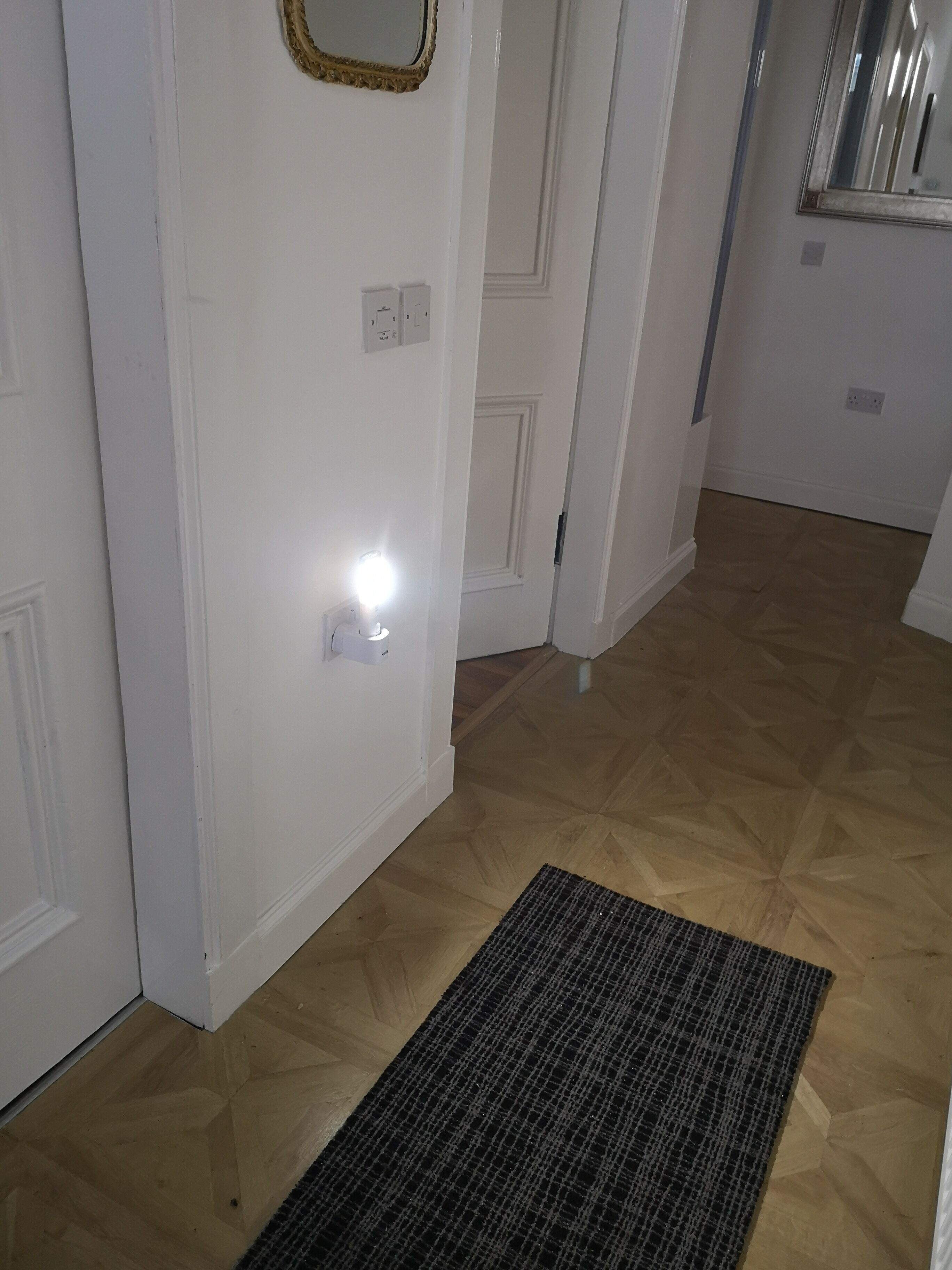 A hallway with a wooden floor, a black textured rug, and white walls.
