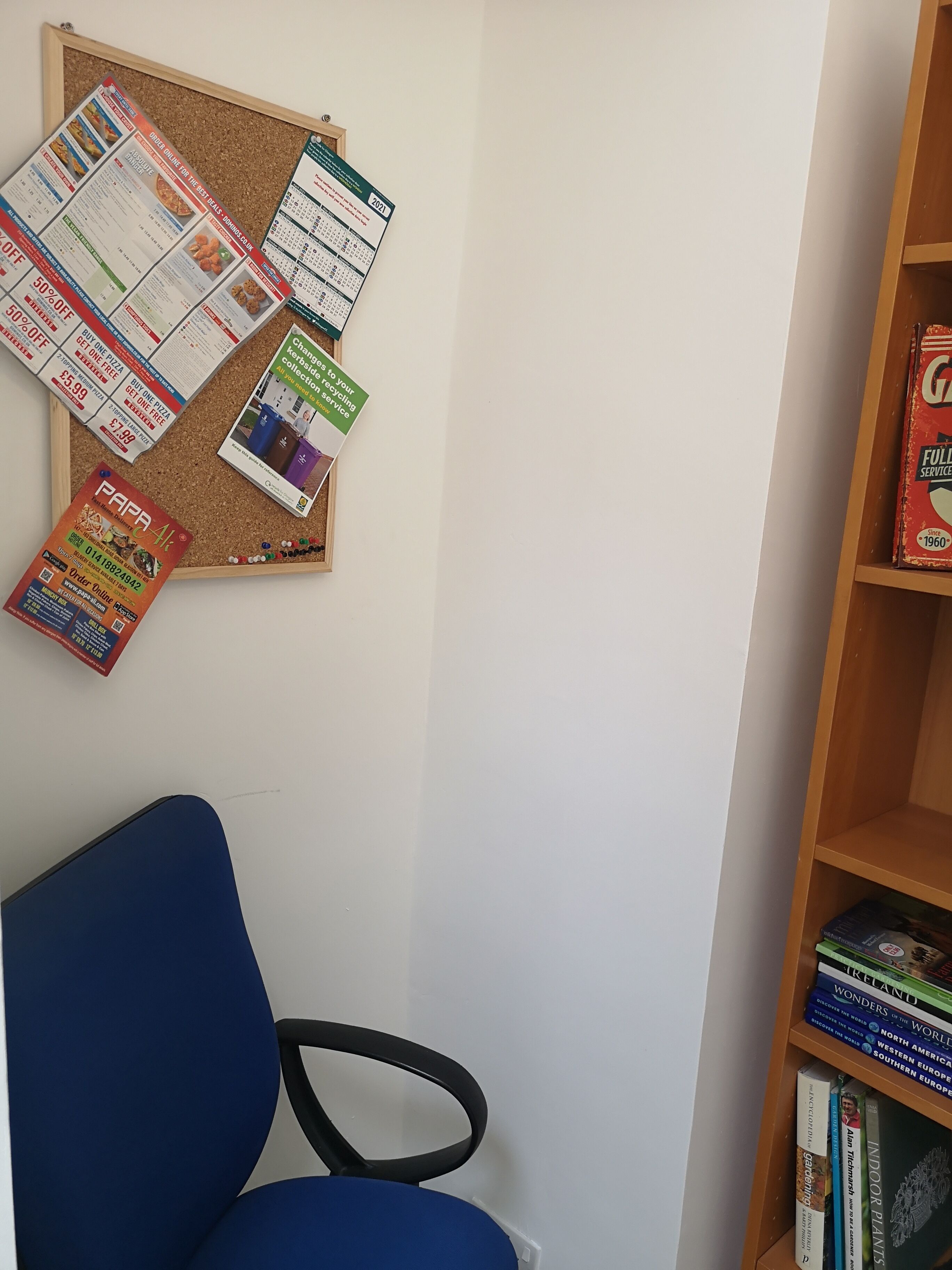 A room with a corkboard displaying various flyers and a bookshelf with books.