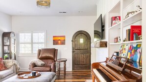 A living room with a piano, a leather armchair, a bookshelf, and a wooden door. - Tennessee Getaway (Jack Daniel’s, Nearest Green) (Shelbyville)