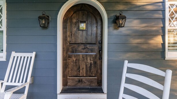 A wooden front door with a white frame, flanked by two white chairs, and two wall-mounted lanterns. - Tennessee Getaway (Jack Daniel’s, Nearest Green) (Shelbyville)