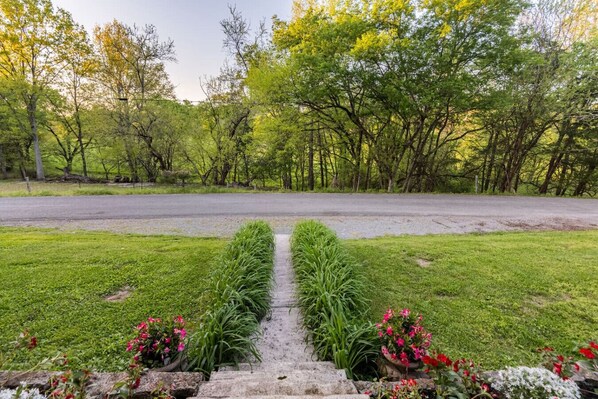 A pathway leading to a road with a grassy area and flowering plants on either side.