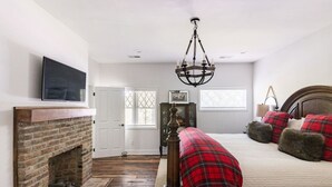 A bedroom with a brick fireplace, a bed with red plaid bedding, and a chandelier. - Tennessee Getaway (Jack Daniel’s, Nearest Green) (Shelbyville)