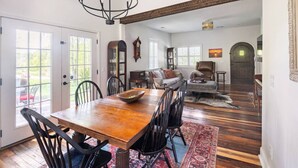 A dining area with a wooden table and chairs, a chandelier, and a view of the outdoors through large windows. - Tennessee Getaway (Jack Daniel’s, Nearest Green) (Shelbyville)