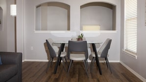A dining area with a table and four chairs, a potted plant, and a window with blinds.