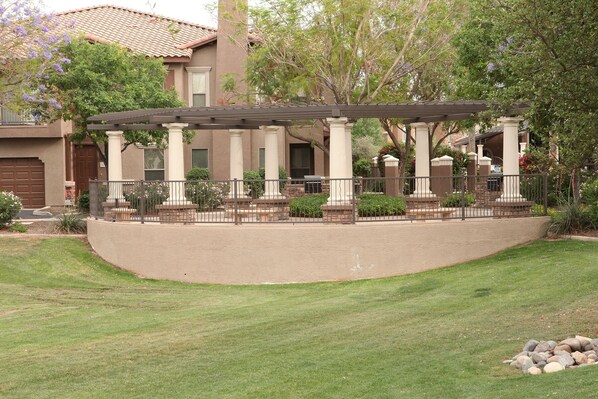 A covered patio with columns, a curved stone wall, and a lawn. - Condominum (Litchfield Park)