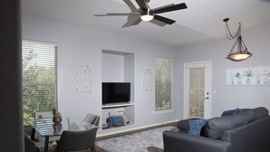 A modern living room with a grey sofa, a glass dining table, and a ceiling fan.
