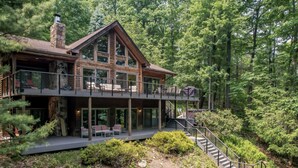 Une cabane en rondins à deux étages, dotée d’un balcon et entourée d’une forêt dense.