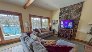 Una sala de estar con un sofá grande, una chimenea de piedra, un televisor y vistas a un cuerpo de agua a través de ventanas amplias.