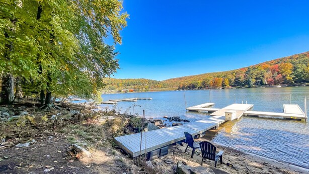 Une jetée au bord du lac, avec une petite embarcation, une terrasse en bois et une vue dégagée sur le lac et les arbres environnants.
