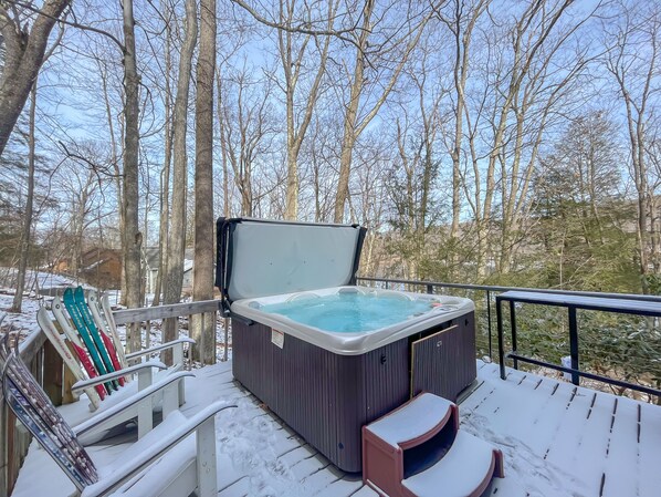Una vasca idromassaggio su un patio con un ponte innevato e una foresta sullo sfondo.