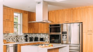 A modern kitchen with wooden cabinets, stainless steel appliances, a large island, and a tiled backsplash. - #3-2BR Shalimar Vacation Townhouse, Frigate Bay, Saint Kitts. (Basseterre)