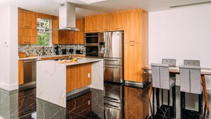 A modern kitchen with wooden cabinets, stainless steel appliances, a marble island, and a dining area with grey chairs. - #3-2BR Shalimar Vacation Townhouse, Frigate Bay, Saint Kitts. (Basseterre)