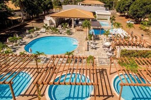 A resort with a large central pool, smaller adjacent pools, and a covered area with umbrellas.