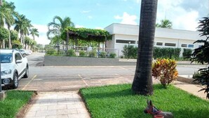 A parking lot with a paved walkway leading to a building entrance, surrounded by palm trees and greenery. - Apartamento de 2/4 no Resort Internacional (caldas novas)