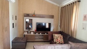 A living room with a flat-screen TV, a brown sofa, a matching ottoman, and a small side table. - Apartamento de 2/4 no Resort Internacional (caldas novas)