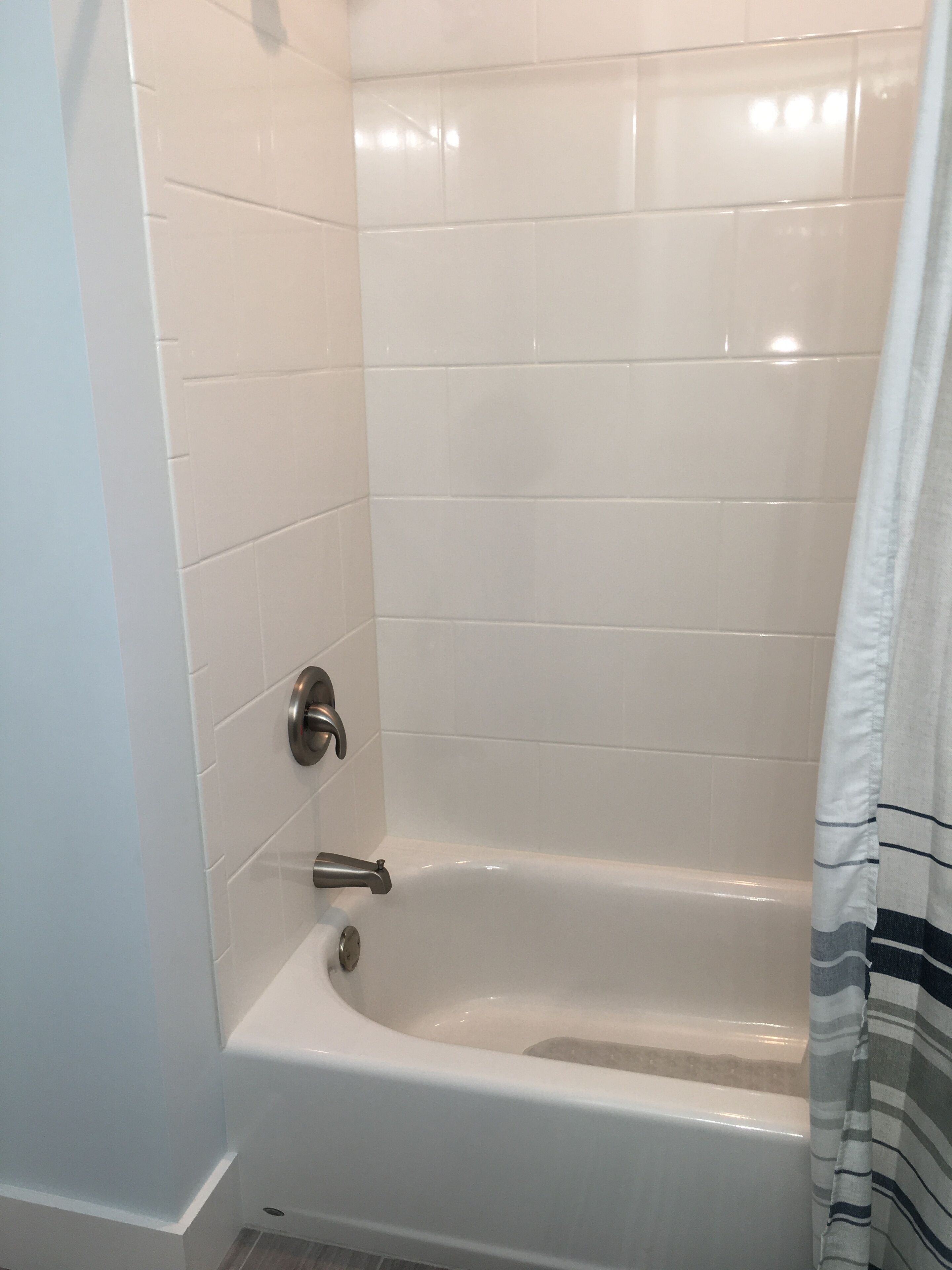 Une salle de bain avec des murs recouverts de carreaux blancs, une baignoire blanche et un rideau de douche.