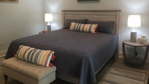 Ein Schlafzimmer mit einem großen Bett, zwei Nachttischen mit Lampen, einer Bank und Kunstwerken an den Wänden.