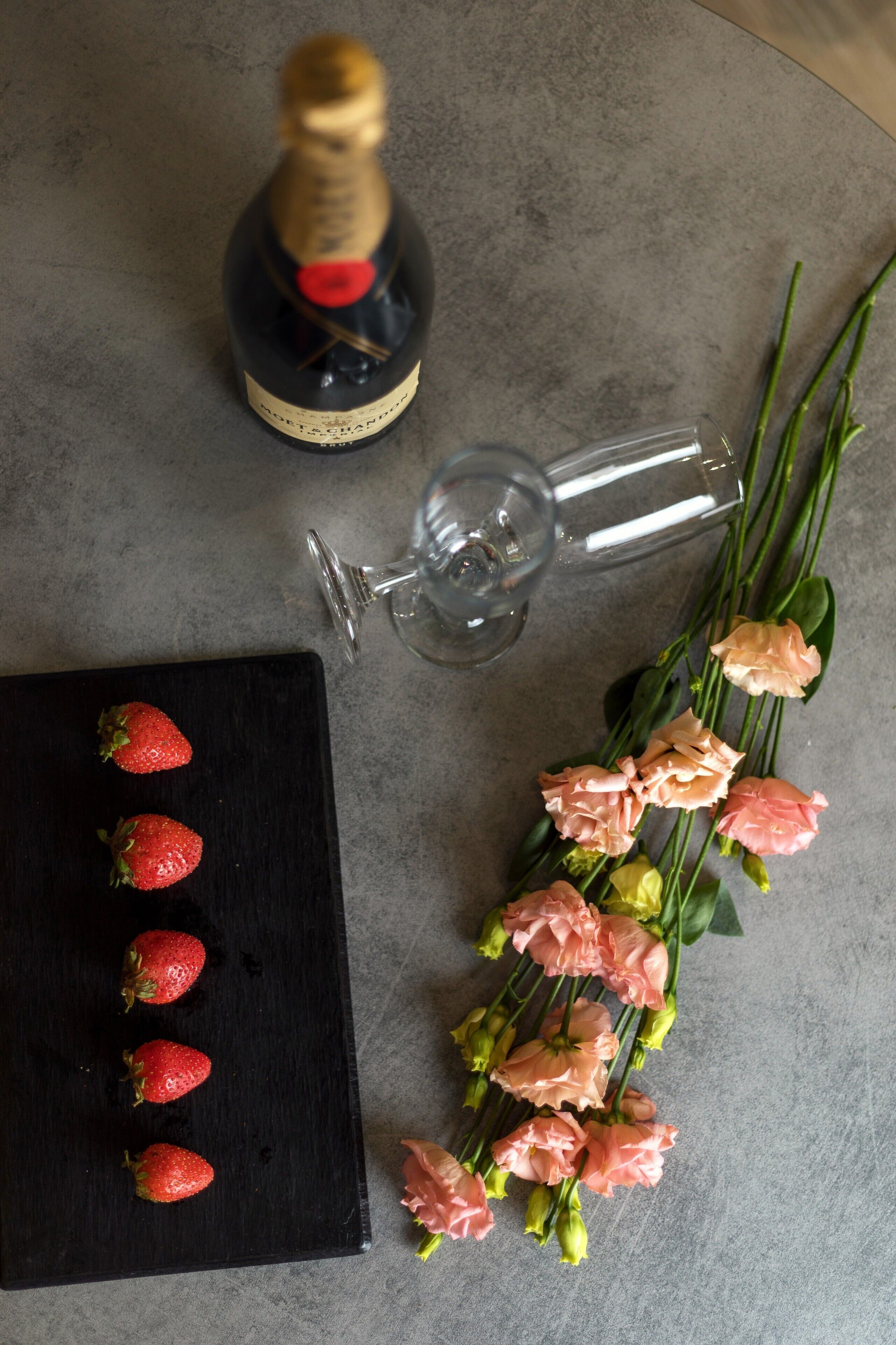 A bottle of champagne, a glass, and a bouquet of flowers on a table.