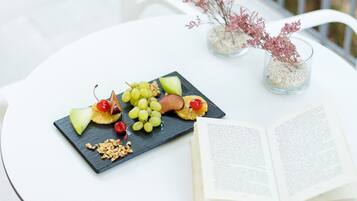 A round white table with a black slate board holding fruit and nuts, an open book, and two glass vases with dried flowers.