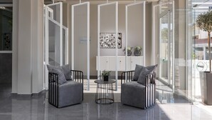 Een modern interieur met een zithoek, bestaande uit twee grijze banken en een kleine ronde tafel, gescheiden door een witte scheidingswand met een gaaspatroon.
