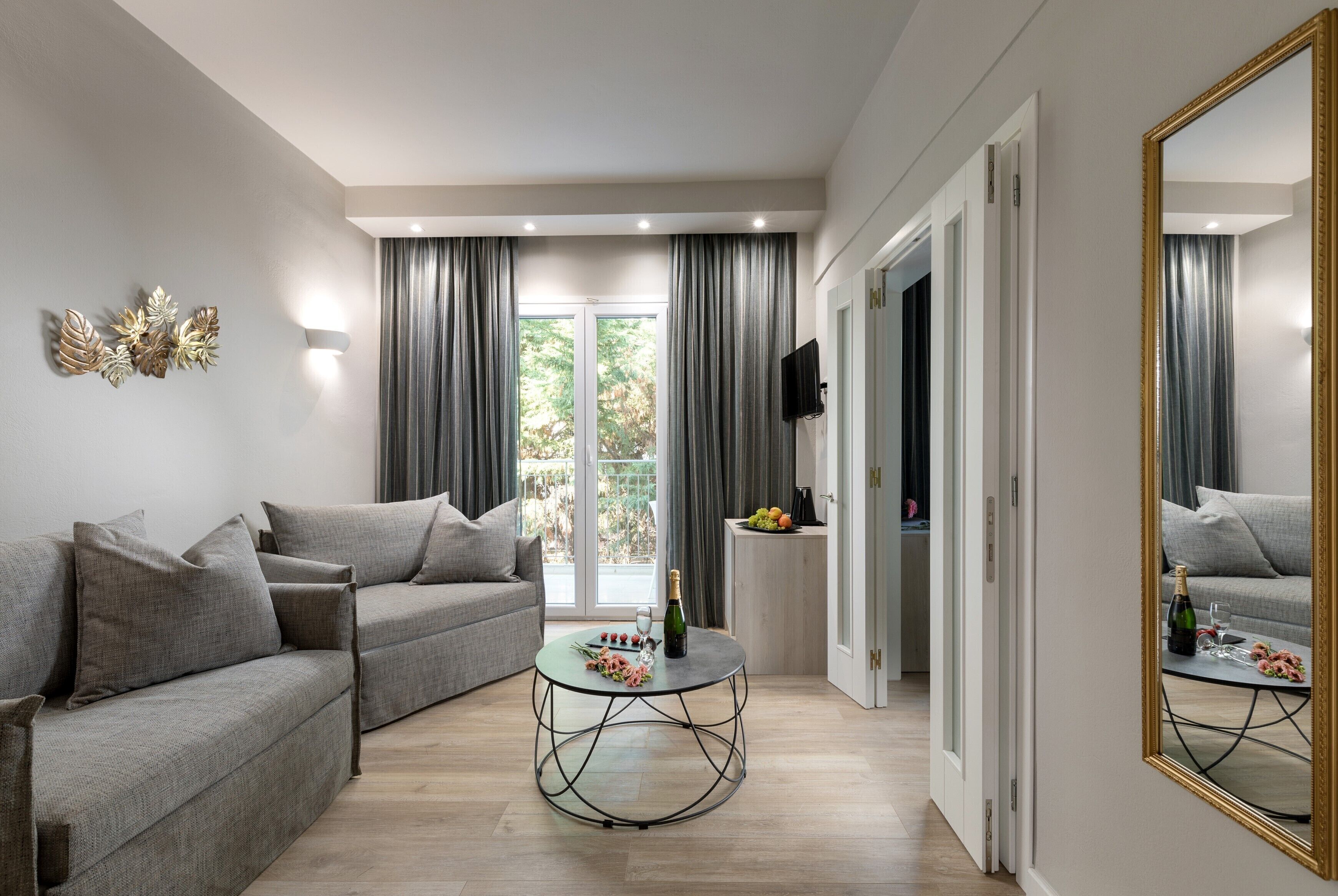 Una sala de estar moderna con un sofá gris, una mesa redonda de centro con flores y un espejo grande.