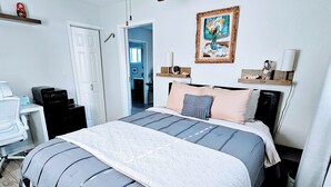 Een slaapkamer met een bed, nachtkastjes, een bureau en een stoel. Er is een deur naar een andere kamer.