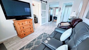 Een woonkamer met een bank, een televisie, een houten dressoir en een kamerkleed met patroon.