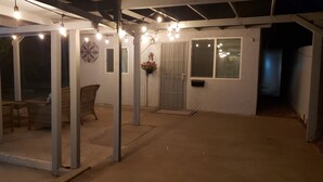 Een overdekt terras met rieten meubels, een metalen hekwerk en hangende lampen.