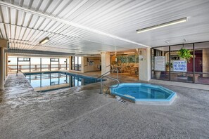 An indoor swimming pool with a lifeguard station, a shallow water warning sign, and a dining area with chairs. - Atalaya Tower 605, Well-maintained Three Bedroom, Two Bath Condo (Garden City Beach)
