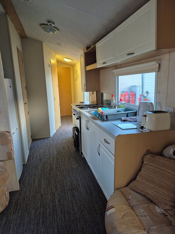 A compact kitchen with a stove, sink, and toaster. There is a window with a view of a building outside.