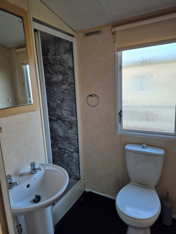 A bathroom with a sink, toilet, and a shower area. - Spacious 8 berth Caravan (Mablethorpe)