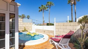 A swimming pool with a hot tub, surrounded by palm trees and a white wall.