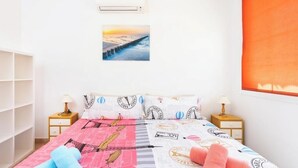 A bedroom with a bed, two bedside tables, a wardrobe, a window with an orange blind, and a picture of a sunset over a bridge.