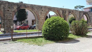 An ancient stone bridge with multiple arches, a paved pathway, and a red car parked nearby. - Camera VENERE (Pisa)