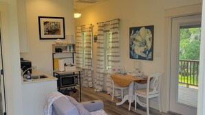 Un salon moderne avec un canapé gris, une table à manger avec des chaises, un ventilateur de plafond et une vue sur la verdure à l’extérieur.