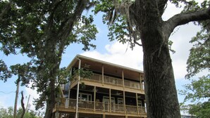 Une cabane en bois à deux étages, dotée d’un balcon et entourée de grands arbres.